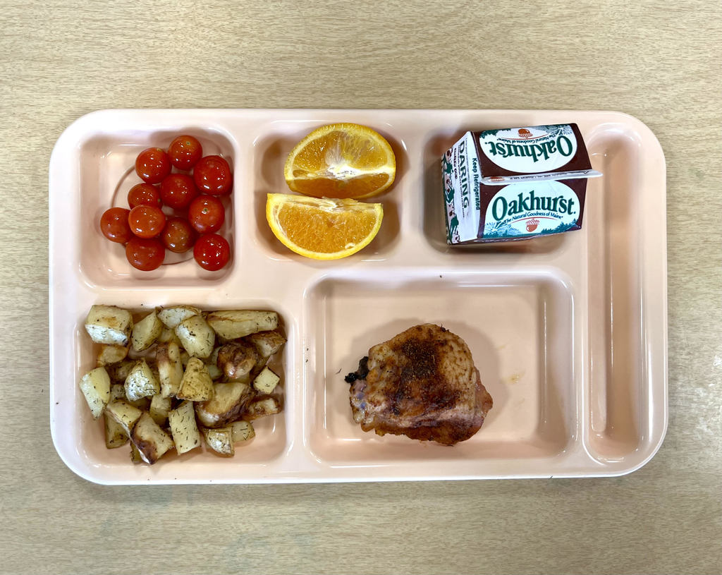 School lunch tray with tomatoes, orange slices, milk, chicken, and potatoes